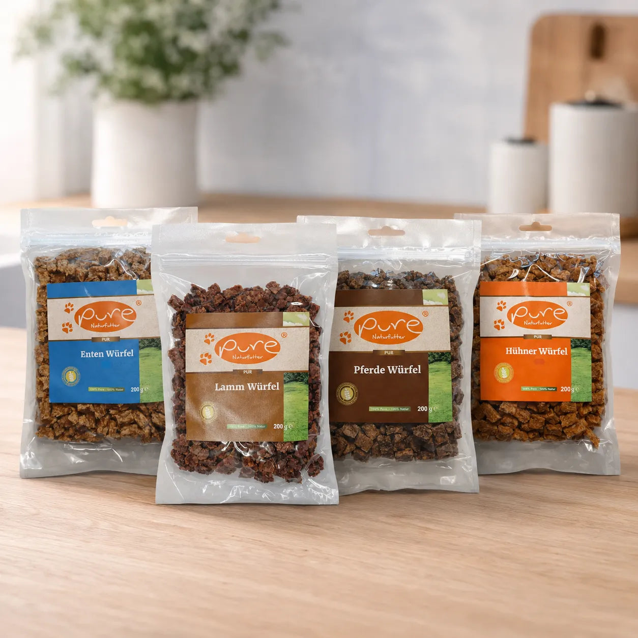 PURE Trainings-Bundle für Hunde mit vier Sorten Mini-Würfel (Ente, Lamm, Pferd, Huhn) auf Holzuntergrund. Getreidefreie Monoprotein-Hundesnacks für das Hundetraining.