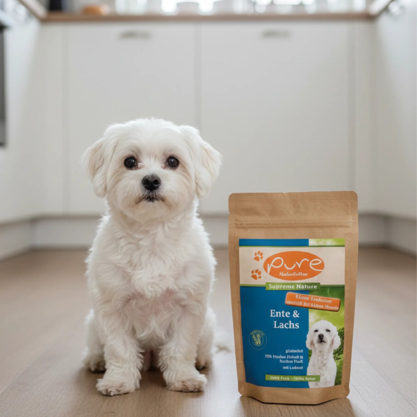 Kleiner Hund sitzt in der Küche neben einem Beutel PURE Ente & Lachs Kleine Kroketten – natürliches Trockenfutter für kleine Hunde