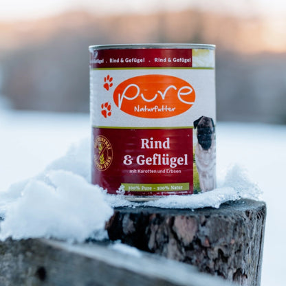 Dose PURE Hundemenü Rind & Geflügel steht im Schnee auf einem Holzpfosten – getreidefreies Nassfutter für Hunde