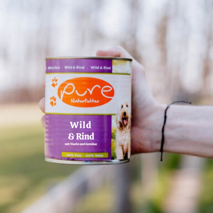 Dose PURE Hundemenü Wild & Rind wird draussen in der Hand gehalten – getreidefreies Nassfutter für Hunde