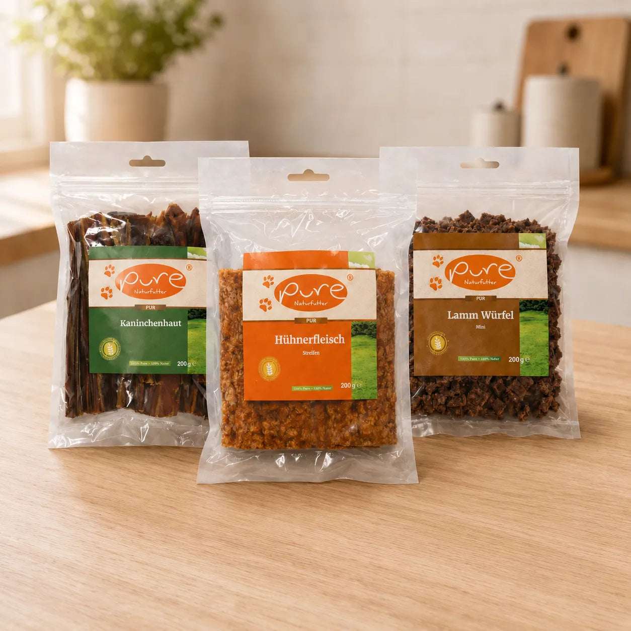 PURE Naturfutter Snack-Bundle mit Kaninchenhaut, Hühnerfleisch Streifen und Lamm Würfel Mini auf heller Küchenarbeitsplatte.